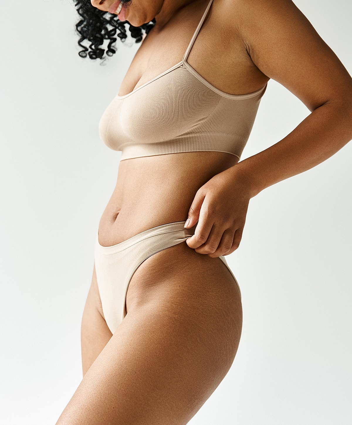 Model wearing beige intimate apparel, side profile.