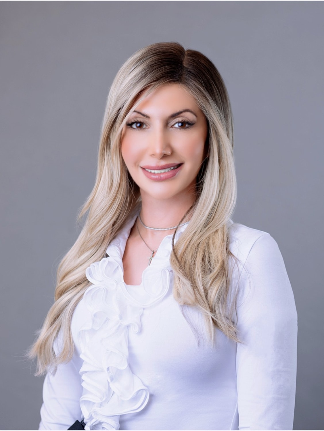 Smiling woman in white blouse against gray background.