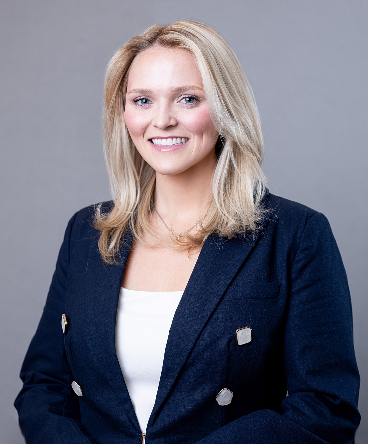Smiling woman in professional attire, gray background.