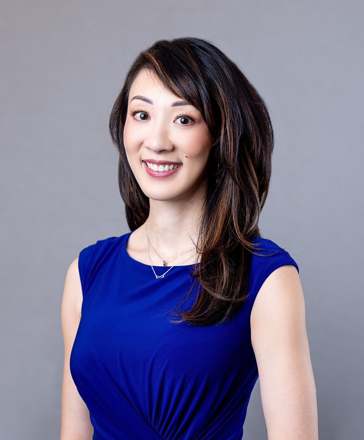 Smiling woman in blue dress against gray background.