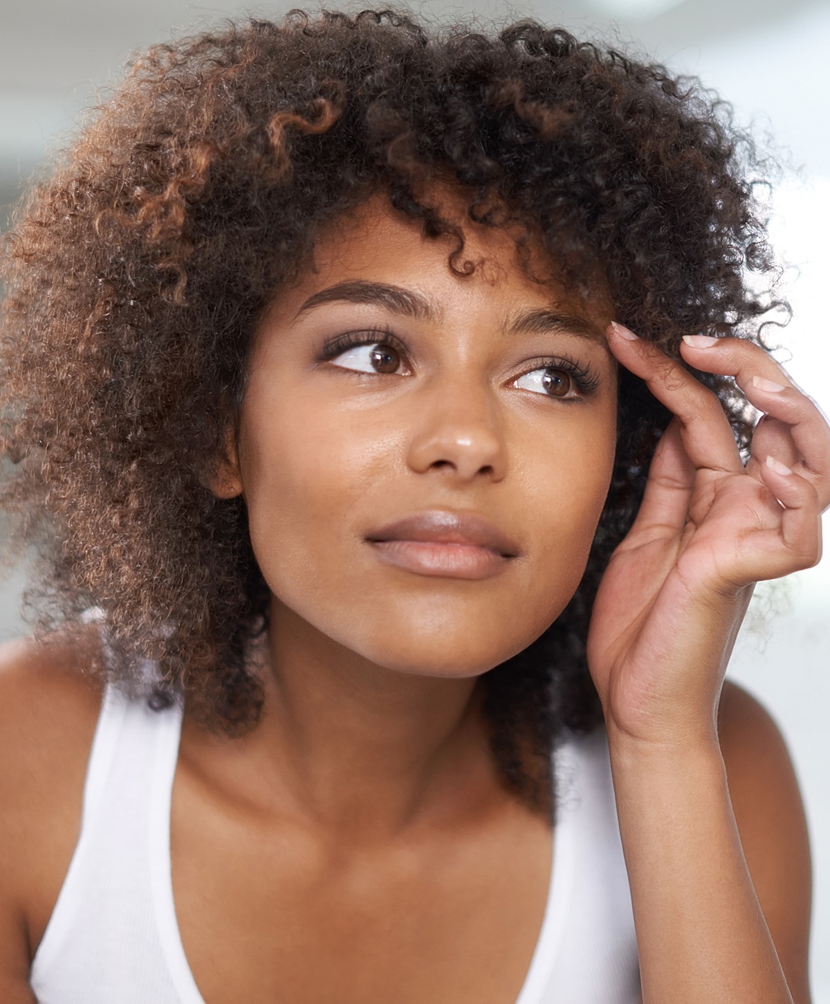 Young woman with curly hair looking thoughtfully.