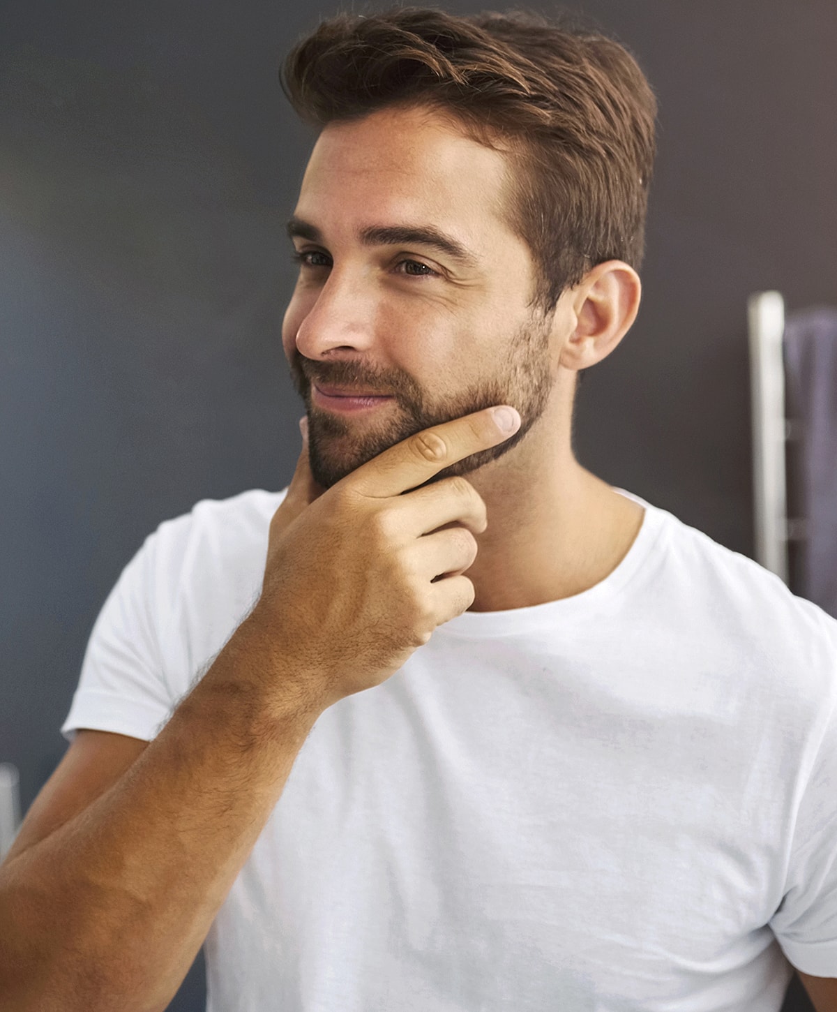 Man thoughtfully stroking his chin in white shirt.