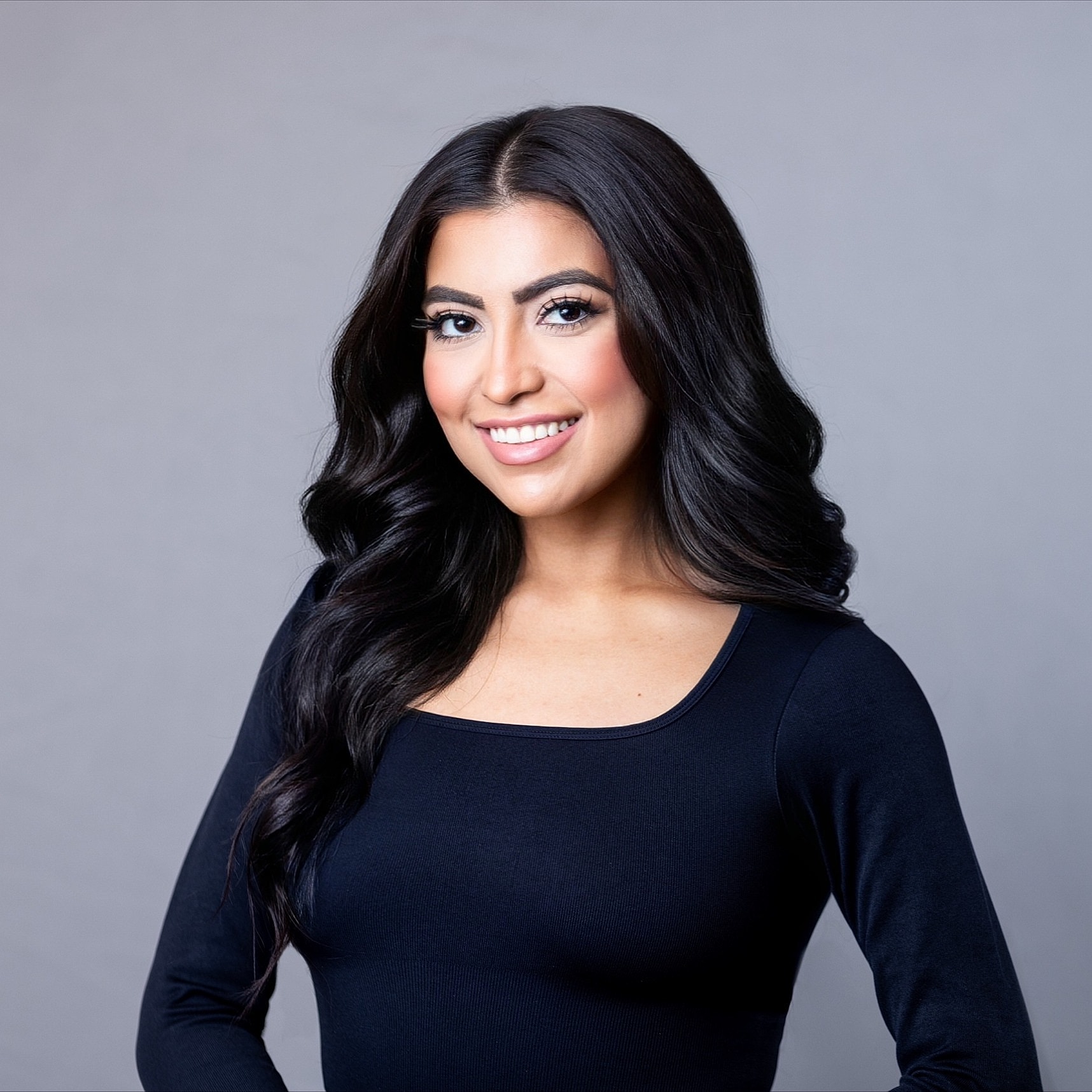 Smiling woman with long dark hair, gray background.