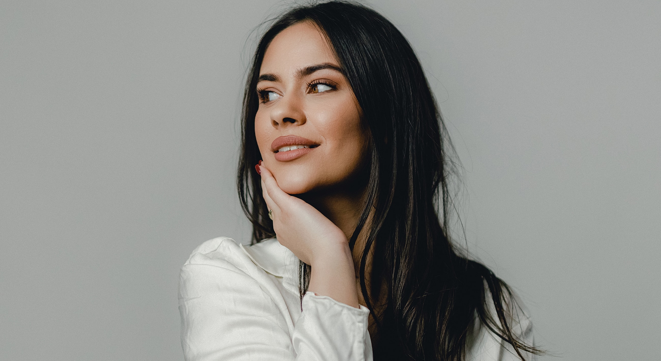 Woman smiling with hand on chin, neutral background.