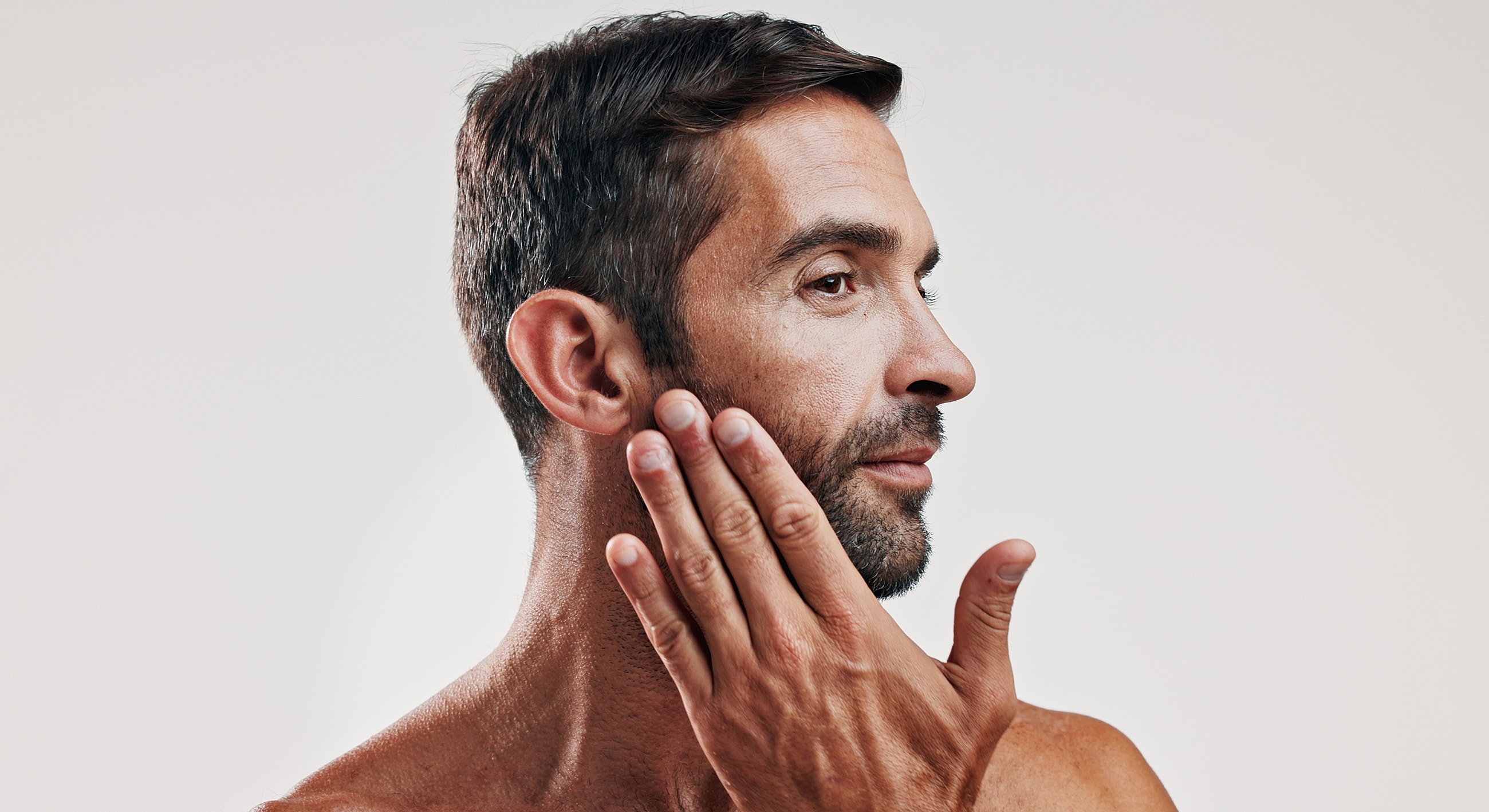 Man touching his face with a neutral background.
