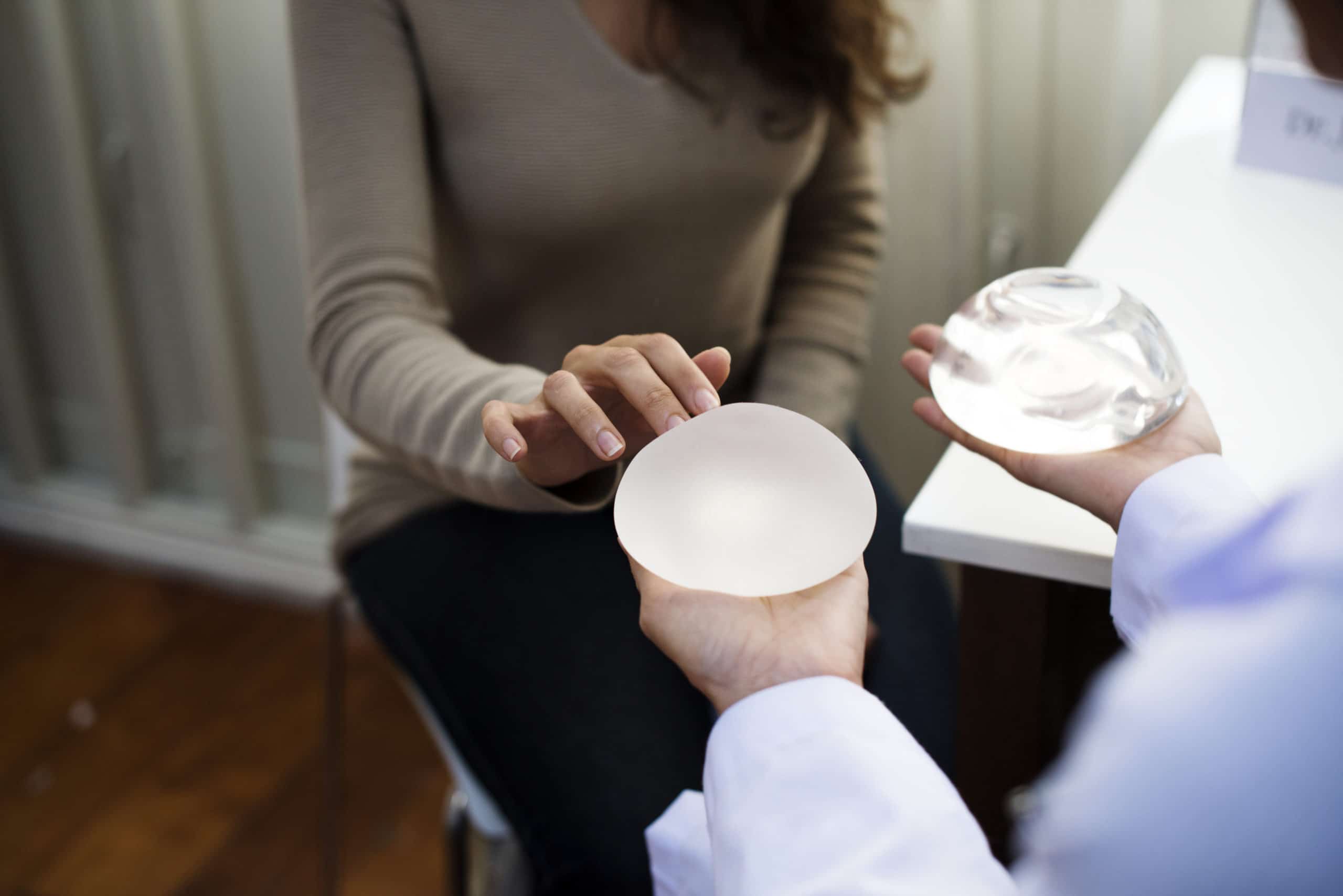 doctor holding both hands out with breast implant in each, one saline, one silicone, showing them to female patient