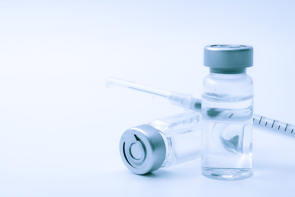 Vaccines, botulin toxin and insulin ampules concept theme with glass vials with clear liquid next to a syringe and a hypodermic needle isolated on white background with copy space a vile of botox concept theme with glass vials with clear liquid next to a syringe and a hypodermic needle isolated on white background