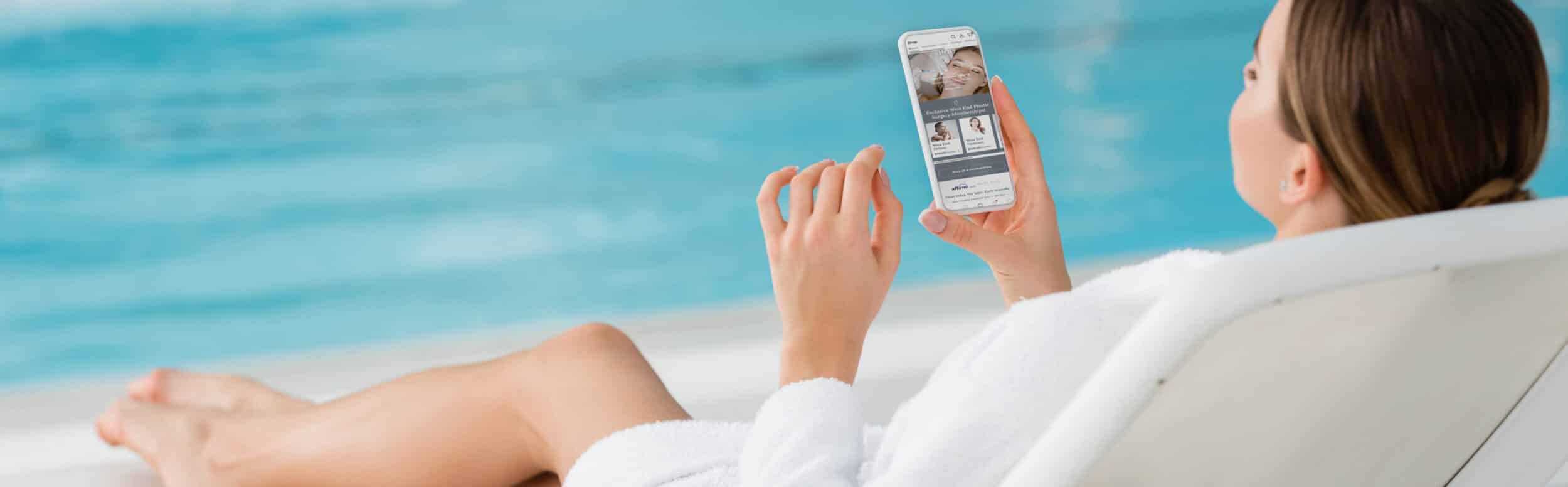 young woman resting on deck chair and holding smartphone with bl
